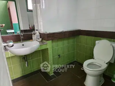Modern bathroom with green and white tiles, featuring a sink and toilet.