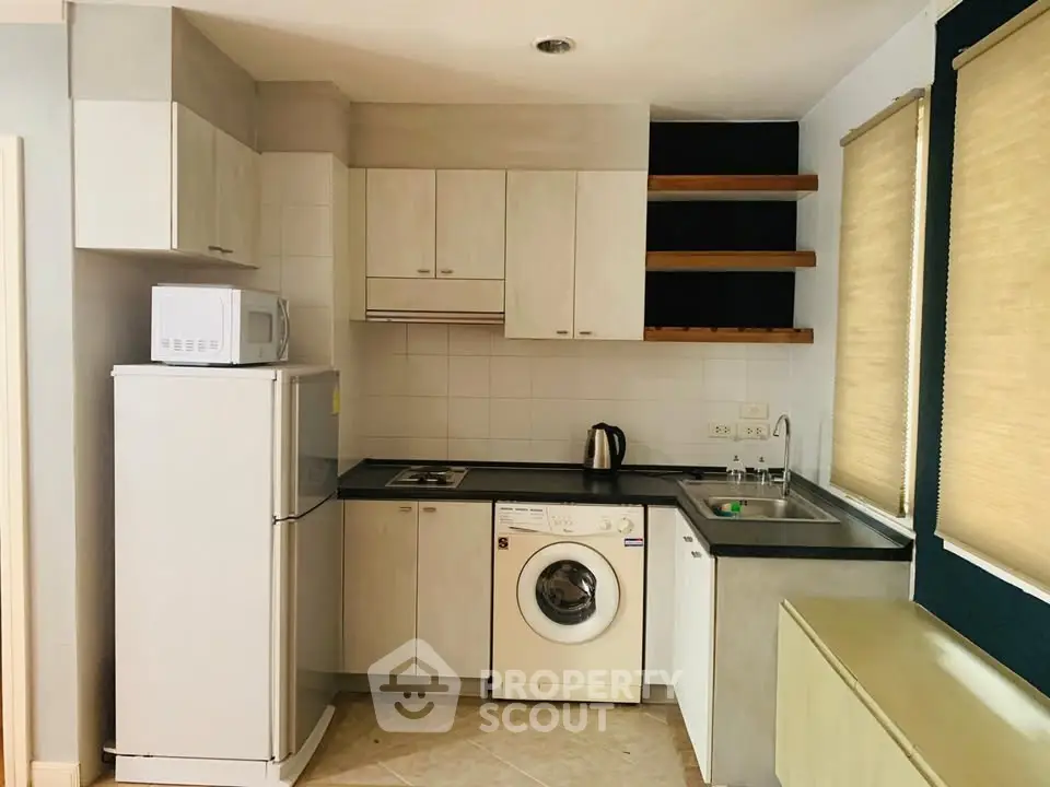 Cozy kitchen with modern appliances including washing machine and microwave, ideal for compact living.