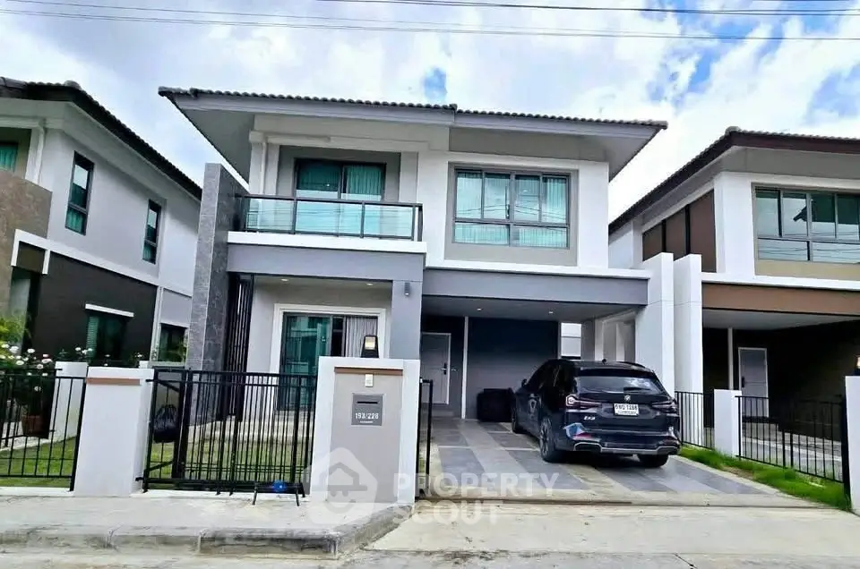 Modern two-story house with driveway and car parked, featuring sleek design and large windows.