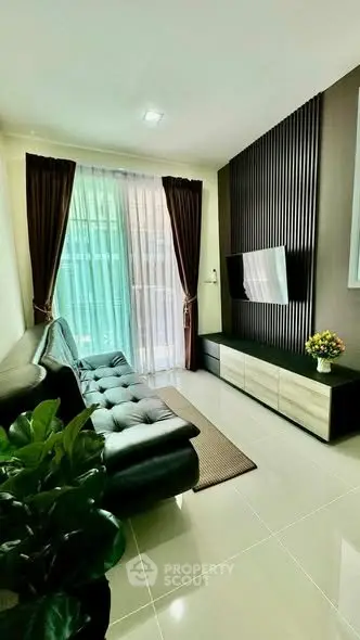 Modern living room with sleek black sofa, wall-mounted TV, and floor-to-ceiling windows for natural light.