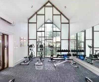Spacious gym with modern equipment and large windows offering natural light.