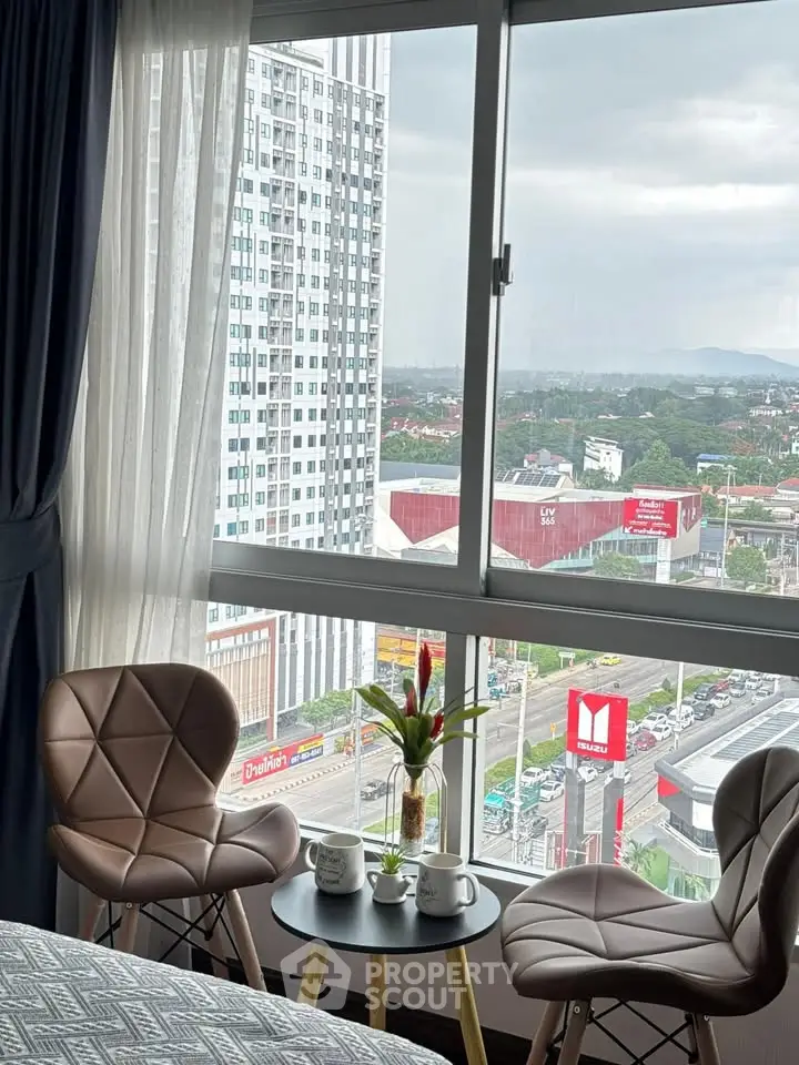 Modern high-rise apartment with stunning city view from large window, featuring cozy seating area.