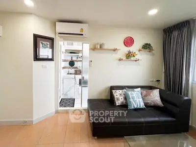 Modern living room with sleek black sofa and stylish decor, featuring a glimpse into a compact kitchen.