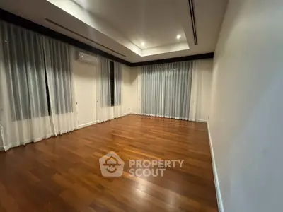 Spacious empty room with wooden flooring and large windows, perfect for customization.