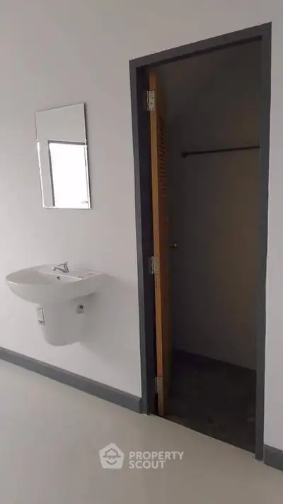 Minimalist bathroom with wall-mounted sink and mirror, featuring a wooden door leading to a small storage area.