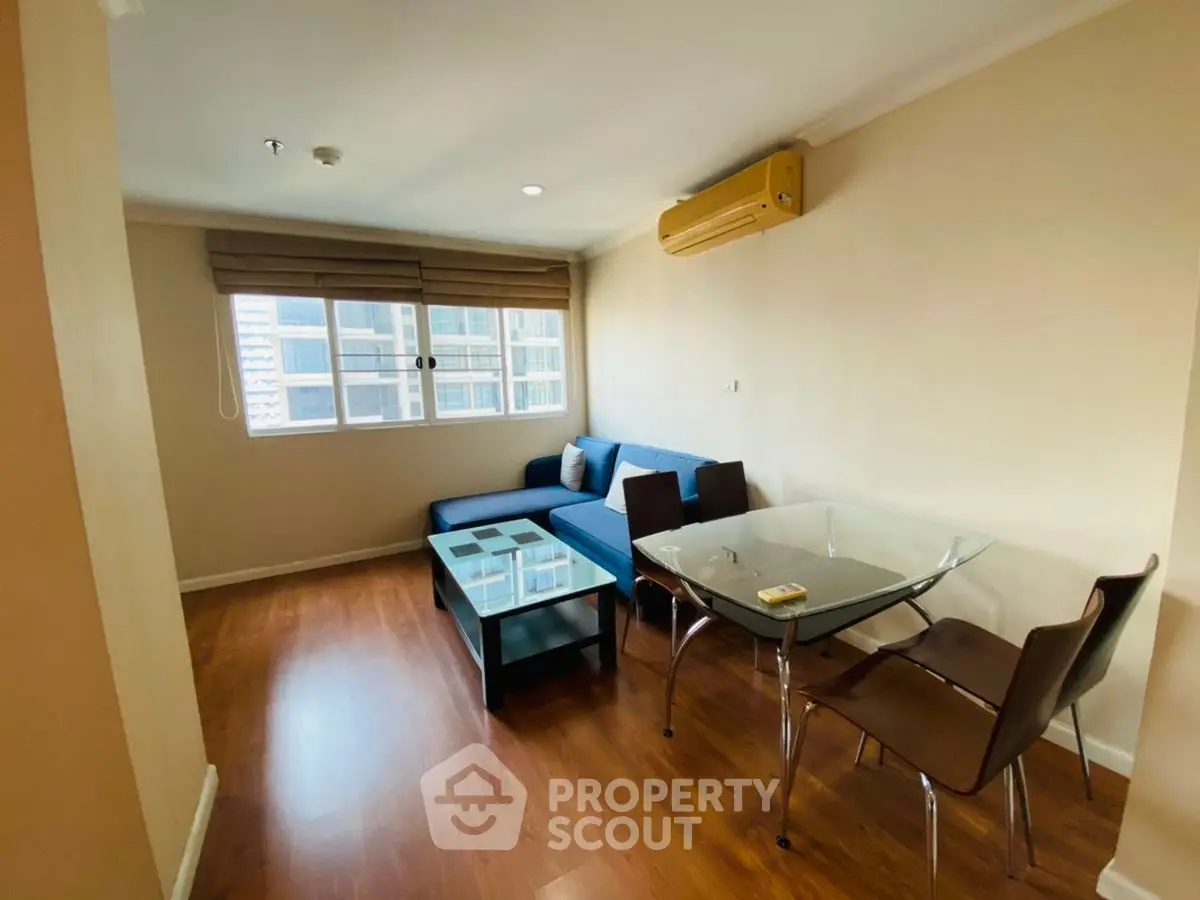 Modern living room with blue sofa and glass dining table in high-rise apartment.