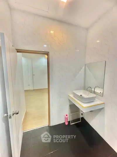 Modern bathroom with sleek sink and mirror, adjacent to a bright hallway with wooden flooring.