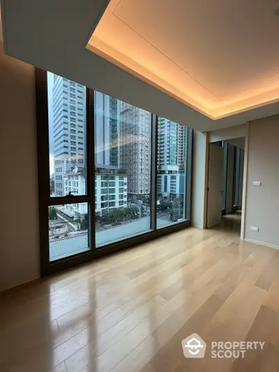 Spacious high-rise living room with floor-to-ceiling windows offering a panoramic city view, accentuated by warm ambient lighting and sleek hardwood floors.