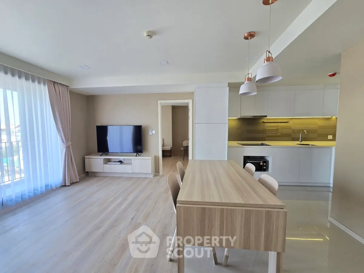 Modern open-plan living room with sleek kitchen and dining area, featuring light wood flooring and contemporary lighting.
