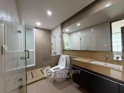 Modern bathroom with glass shower, sleek vanity, and large mirror in contemporary apartment.