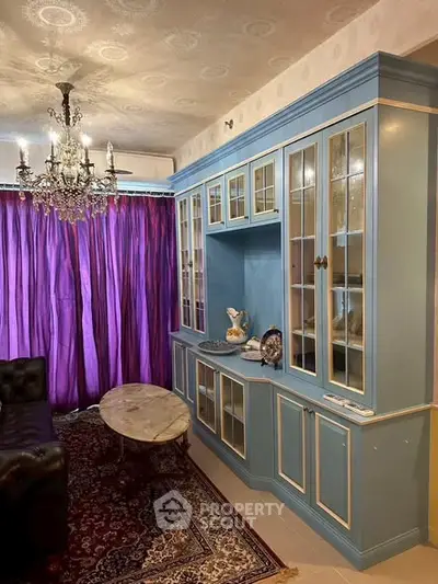 Elegant living room with vintage chandelier, blue cabinetry, and luxurious purple curtains.
