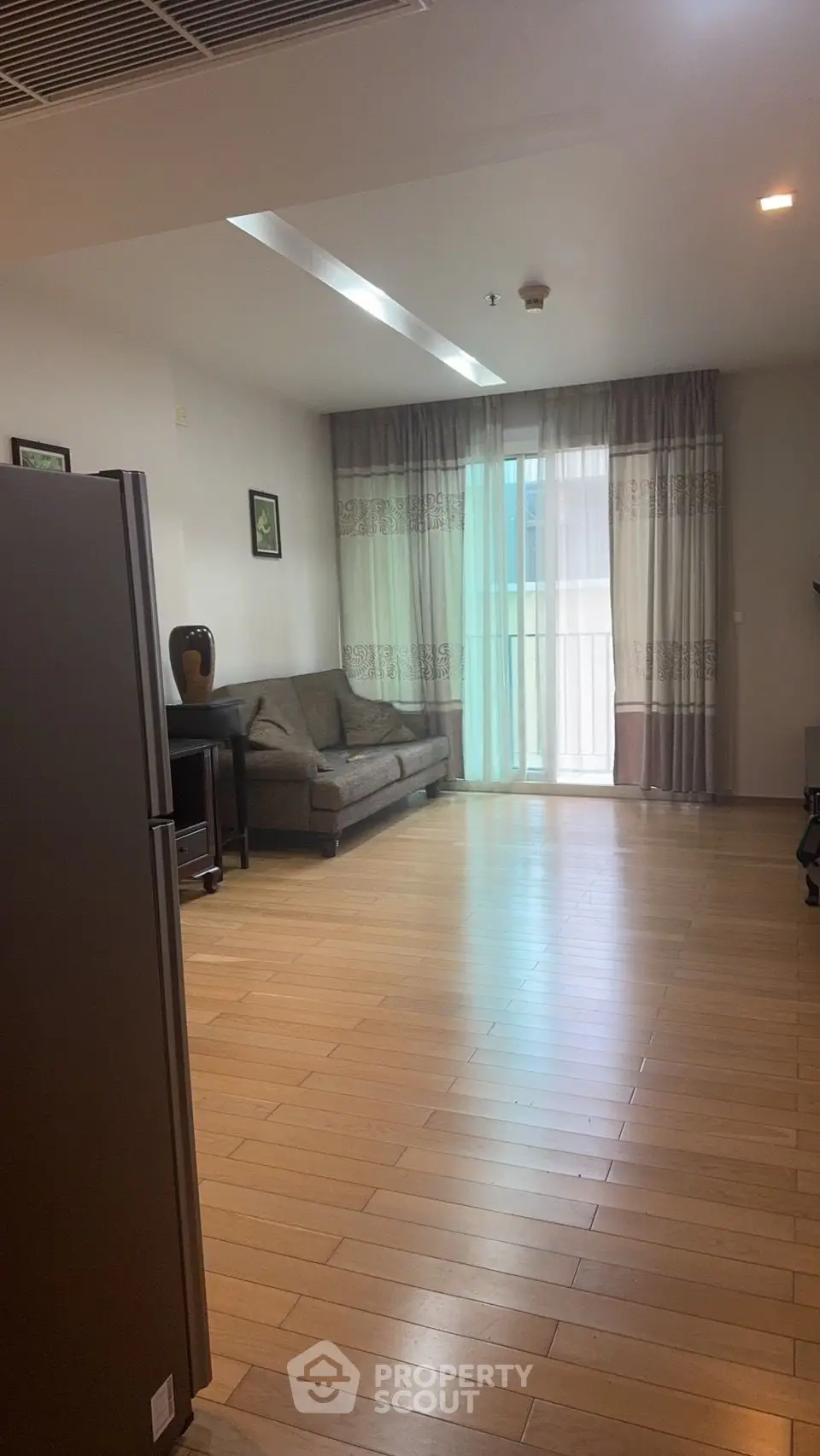 Spacious living room with wooden flooring and natural light from large windows.