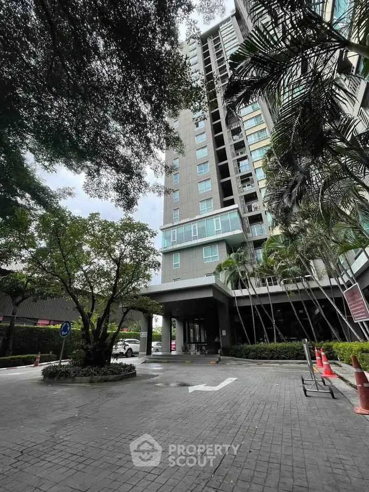 Modern high-rise building exterior with lush greenery and spacious entrance.