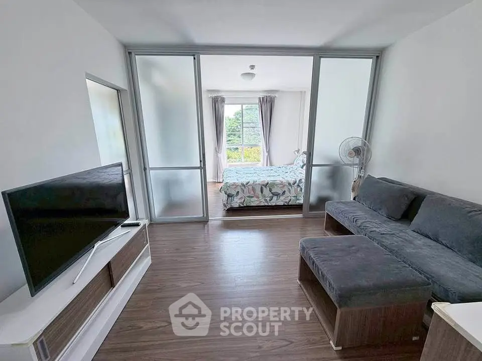 Modern apartment with open living room and bedroom, featuring sleek furniture and natural light.