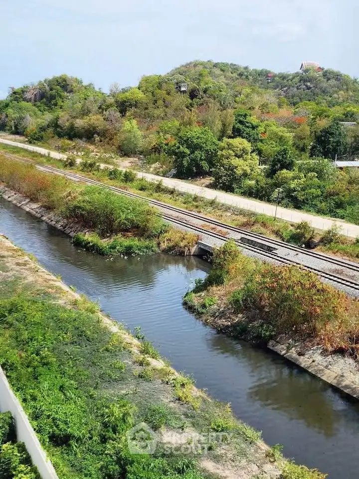 Scenic view of lush greenery and railway track near a serene waterway, perfect for nature lovers.
