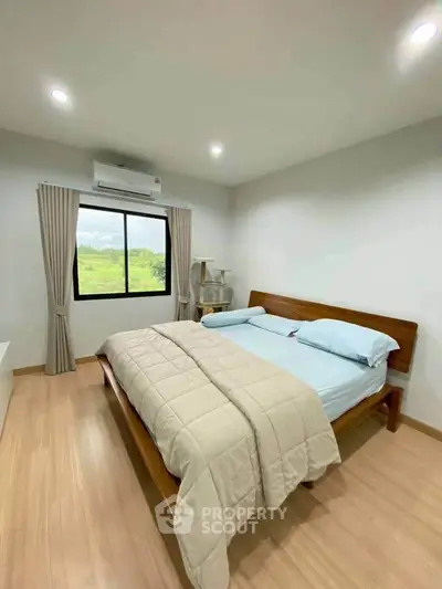 Cozy bedroom with wooden flooring and large window offering scenic views.