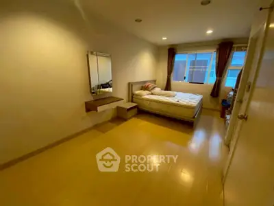 Spacious bedroom with wooden flooring and natural light, featuring a comfortable bed and wall-mounted mirror.