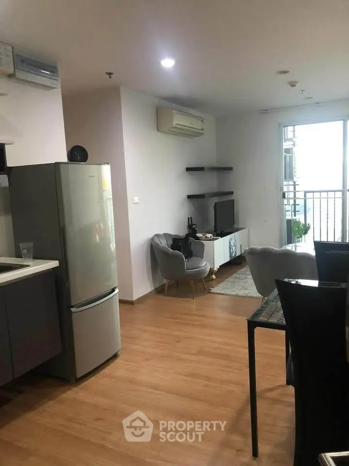 Modern open-plan living room with sleek kitchen and balcony access, featuring stylish furniture and wooden flooring.