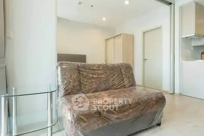 Modern living room with plastic-covered sofa and glass side table in bright apartment.