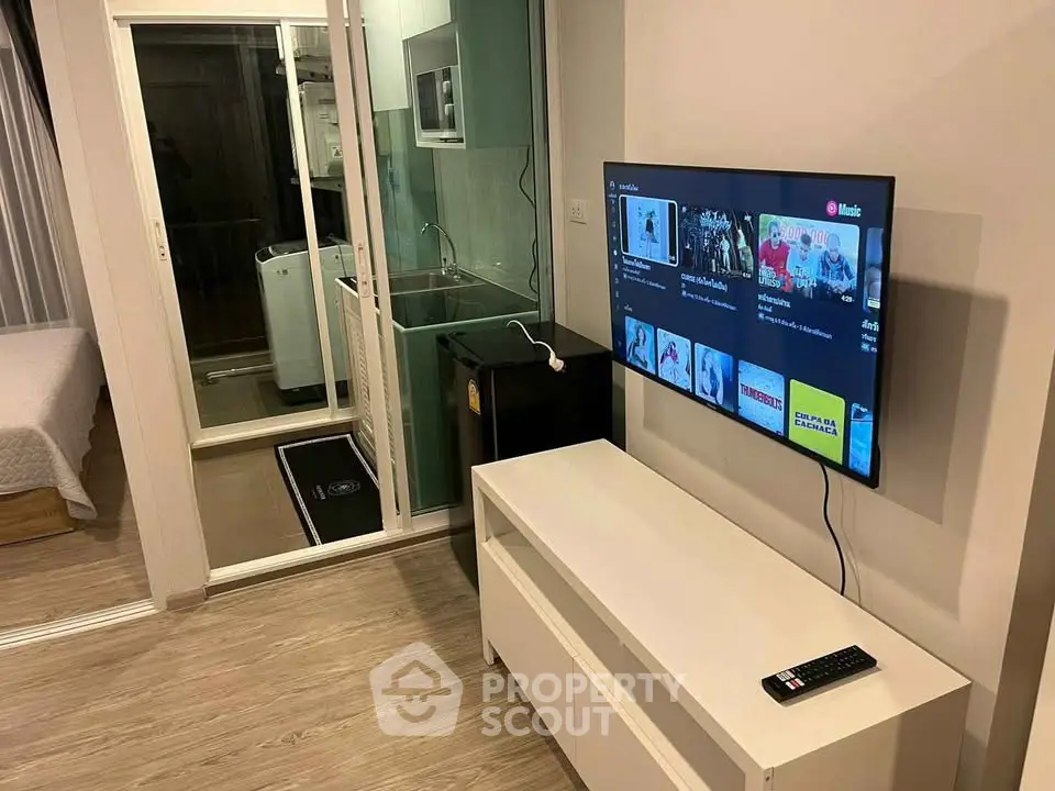 Modern apartment interior with TV, kitchen, and washing machine, showcasing open layout and sleek design.