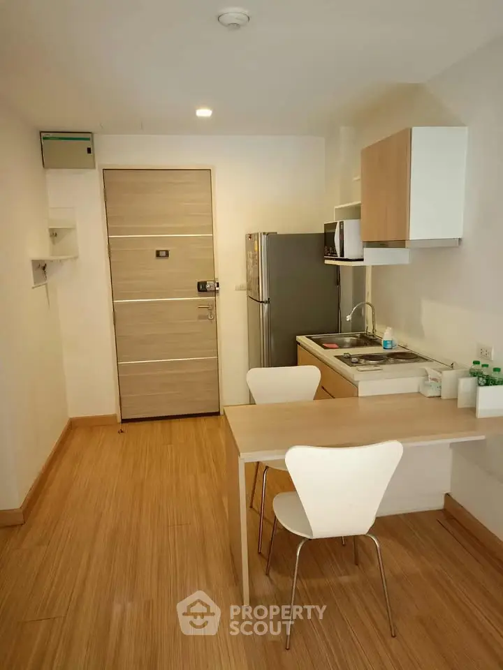 Modern compact kitchen with wooden flooring and sleek appliances in a cozy apartment.