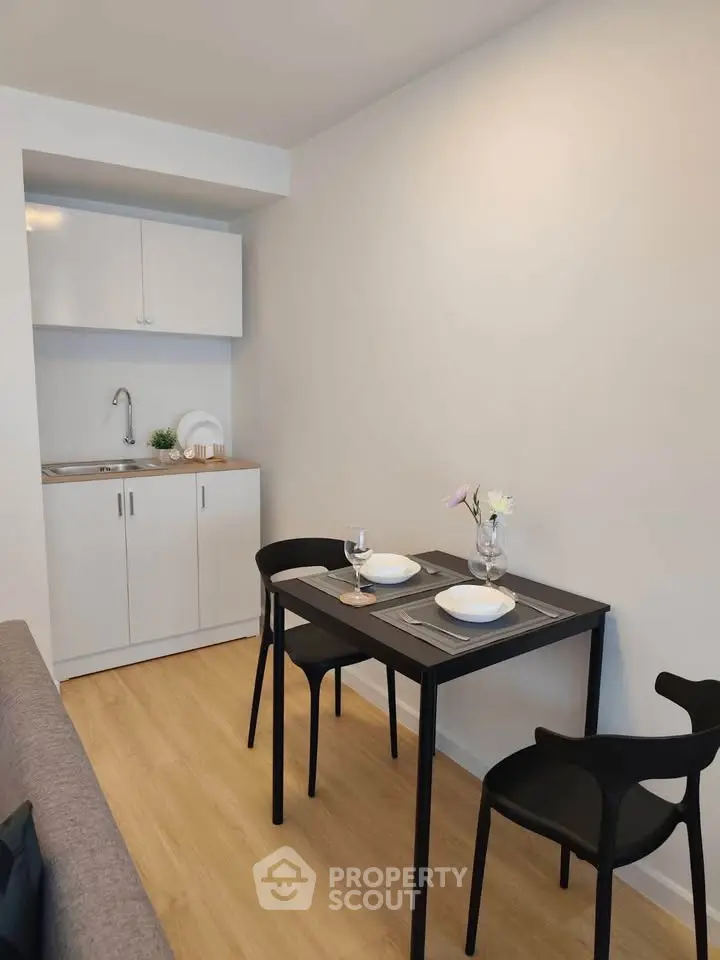 Modern compact dining area with sleek black table and chairs, adjacent to a minimalist kitchenette.