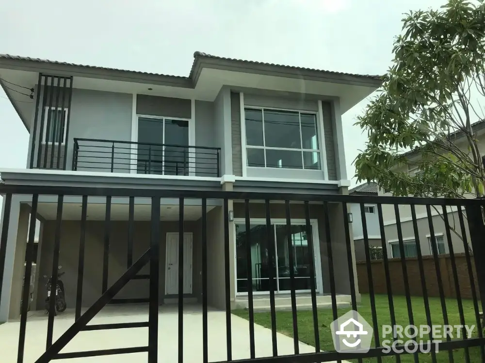 Modern two-story house with large windows and gated entrance in suburban neighborhood.