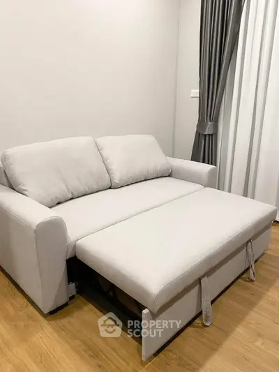 Modern living room with sleek gray sofa bed and elegant curtains on wooden flooring.