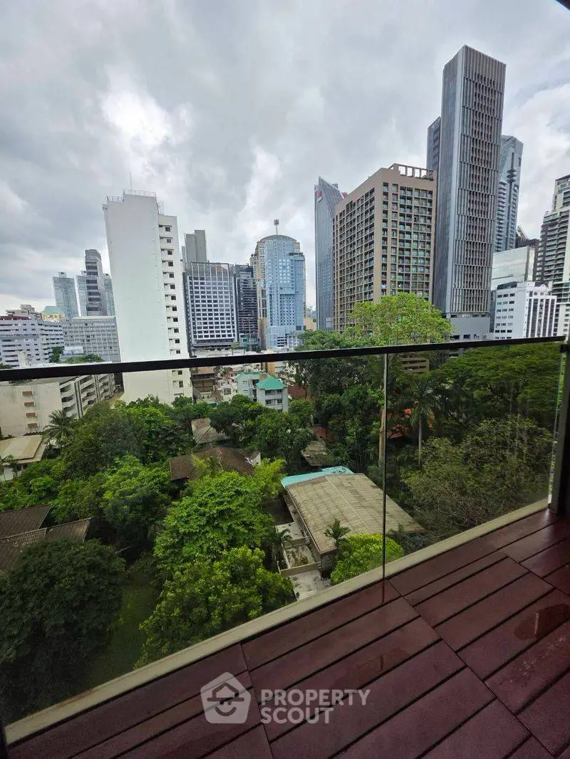 Stunning cityscape view from a modern balcony with glass railing, showcasing lush greenery and skyscrapers.