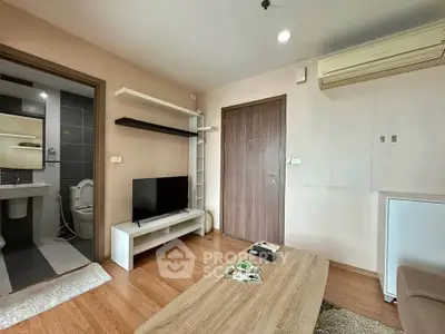 Modern living room with wooden flooring, TV, and air conditioning, adjacent to a sleek bathroom.