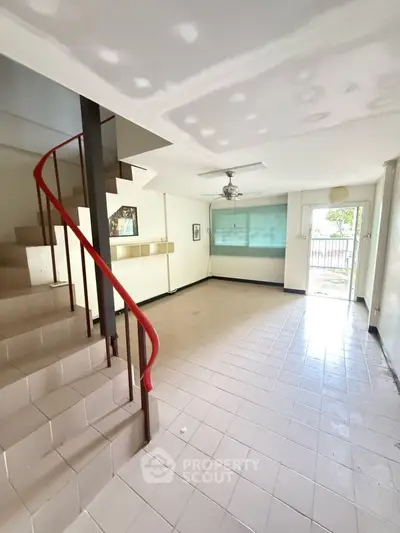 Spacious living room with staircase and large window, ideal for family gatherings.