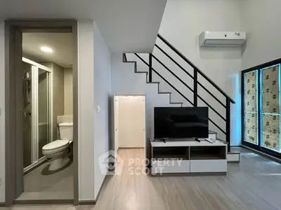 Modern duplex living room with staircase, TV unit, and bathroom access.