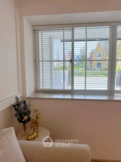 Cozy living room corner with window view of colorful houses, featuring elegant decor and natural light.