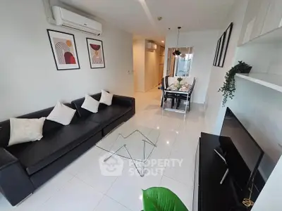 Modern living room with sleek black sofa, glass coffee table, and stylish wall art in a bright apartment.