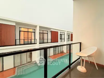 Modern balcony overlooking pool with stylish chair and glass railing