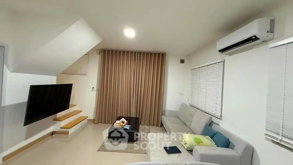 Modern living room with sleek design, featuring a cozy sofa, wall-mounted TV, and air conditioning.