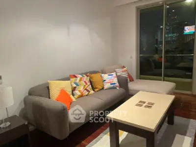 Modern living room with colorful cushions and city view balcony at night.