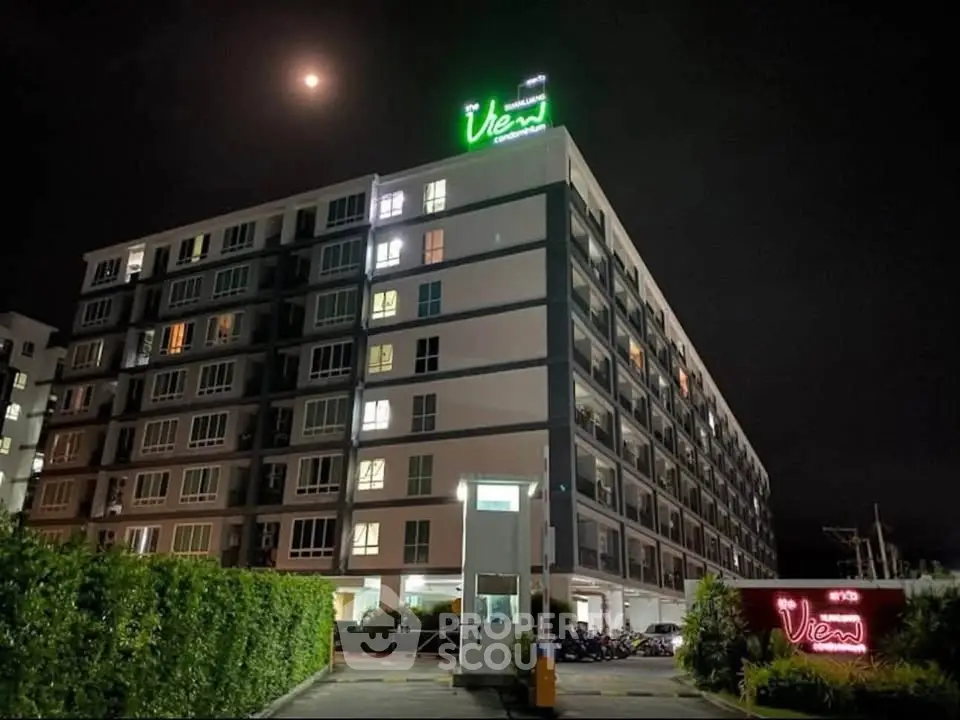 Modern apartment building at night with illuminated signage and lush greenery.