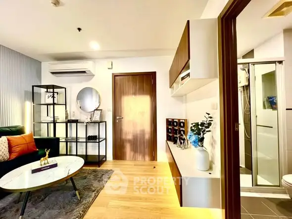 Modern living room with stylish decor and adjacent bathroom, featuring sleek furniture and warm lighting.