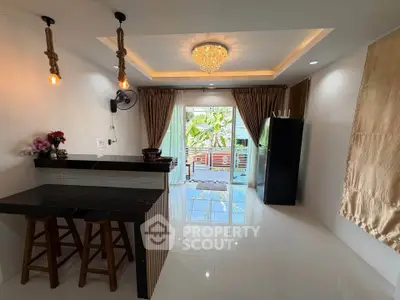 Modern kitchen with open layout and stylish lighting, featuring a breakfast bar and large windows with garden view.
