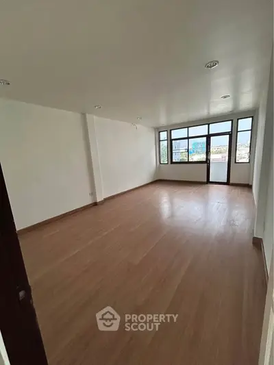 Spacious empty room with large windows and wooden flooring, offering a bright and airy atmosphere.