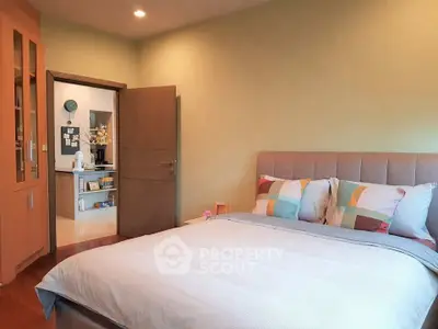 Cozy bedroom with modern decor and colorful pillows, leading to a stylish kitchen.