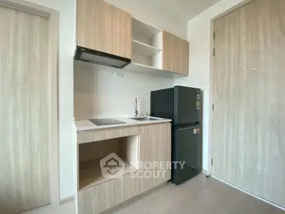Modern compact kitchen with sleek wooden cabinets and black fridge in a minimalist apartment.