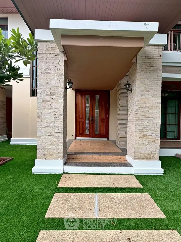 Elegant entrance of a modern home with stone pillars and lush green lawn.