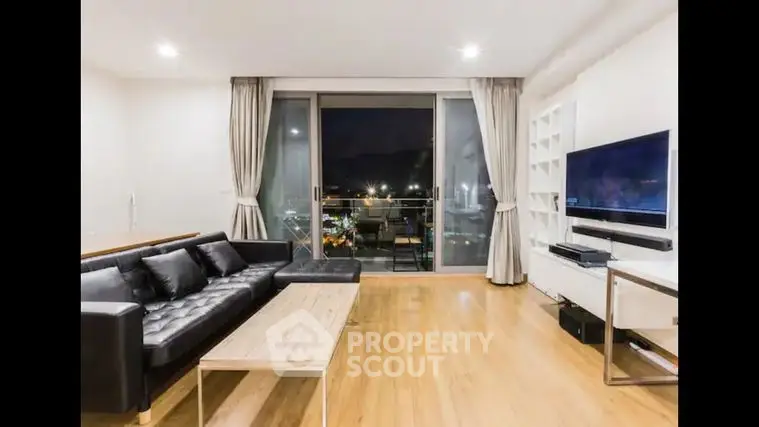 Spacious living room with polished hardwood floors, modern furniture, and large windows offering a stunning night view, perfect for urban living.