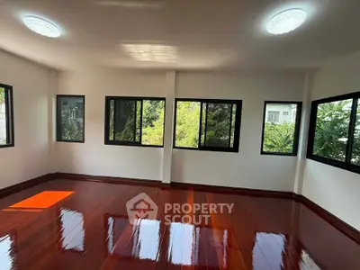 Spacious room with polished wooden floors and large windows offering lush green views.