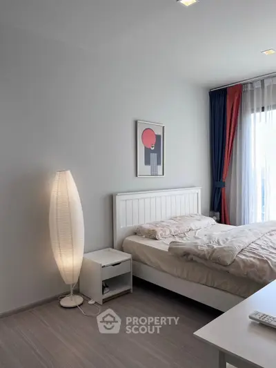 Modern bedroom with stylish decor and natural light, featuring a cozy bed and elegant floor lamp.