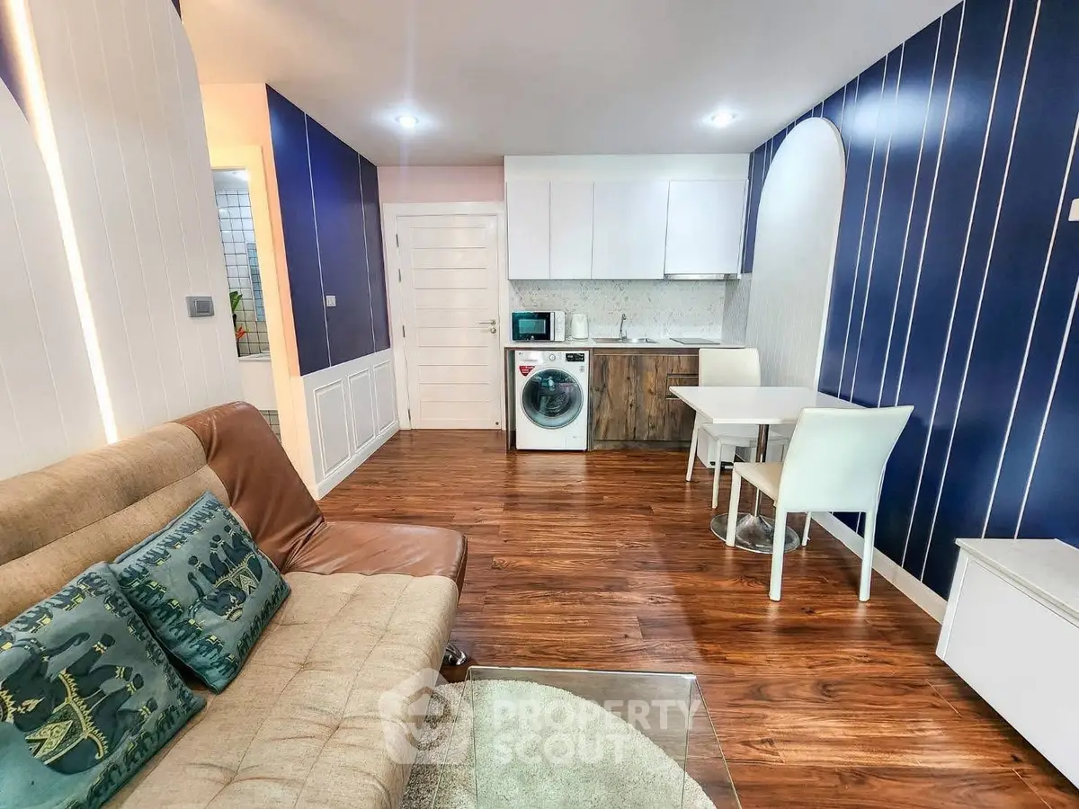 Modern living room with open kitchen and washing machine, featuring stylish decor and wooden flooring.