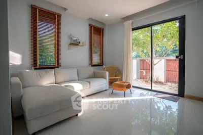 Bright living room with large windows and cozy sofa, opening to a lush garden view.