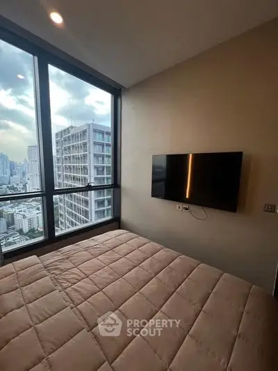 Modern bedroom with city view and wall-mounted TV in high-rise apartment.